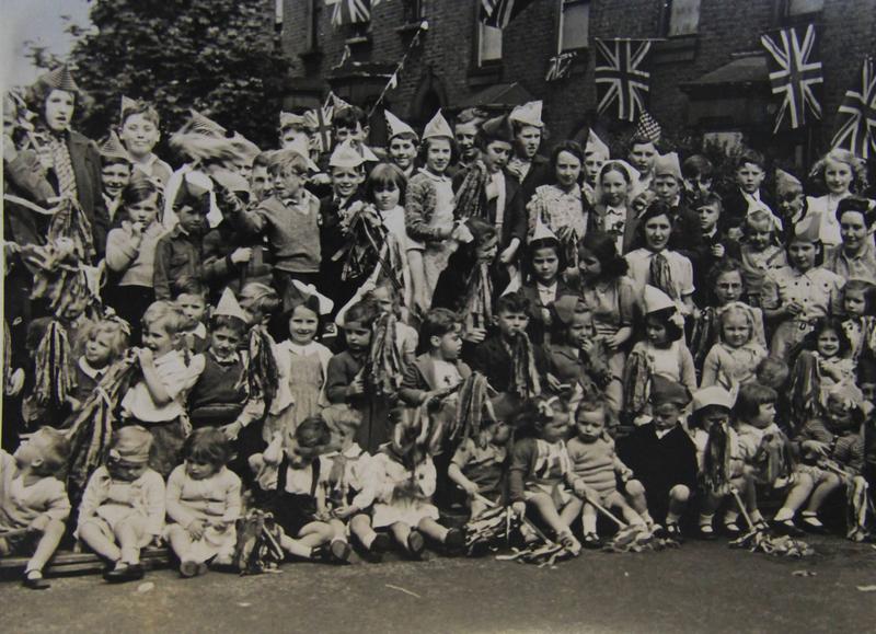 hackney street party - group photo of children on VE day wearing party hats and waving streamers