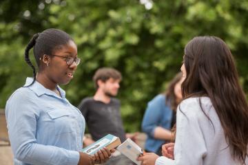 Two students outside talking with books in their hands