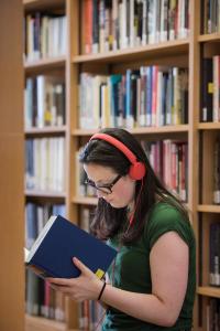 Student wearing orange headphones reading a book in a library